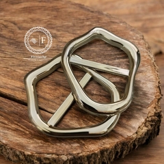 Fivela metal dourado modelo orgânica, com design moderno, sobre uma superfície de madeira.