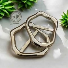 Fivelas ABS modelo Fi/Passante na cor dourada, pacote com 6 peças, sobre fundo claro com plantas decorativas.