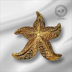 Fivela de metal em formato de estrela do mar na cor dourada, com textura detalhada.
