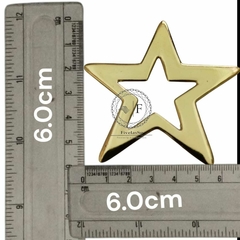 Fivela de metal em formato de estrela, com duas alças, medindo 6 cm de largura, ao lado de uma régua para referência de tamanho.