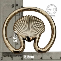 Fivela modelo concha circular em ABS na cor dourada, com medidas de 5,0 cm e 5,5 cm, sobre uma régua.
