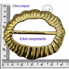 Fivela orgânica dourada com detalhes em metal, medindo 4,8 cm de largura e 6,0 cm de comprimento.