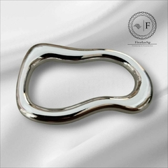 Fivela orgânica simples em metal com design curvado, em fundo branco.