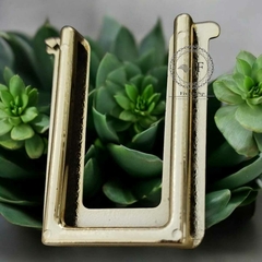 Fivela plástica modelo U na cor dourada sobre fundo verde, mostrando detalhe da abertura de 4cm.