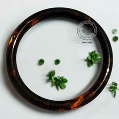 Par de alças de resina redonda na cor caramelo escuro, destacando-se sobre uma superfície branca com pequenas plantas verdes ao redor.