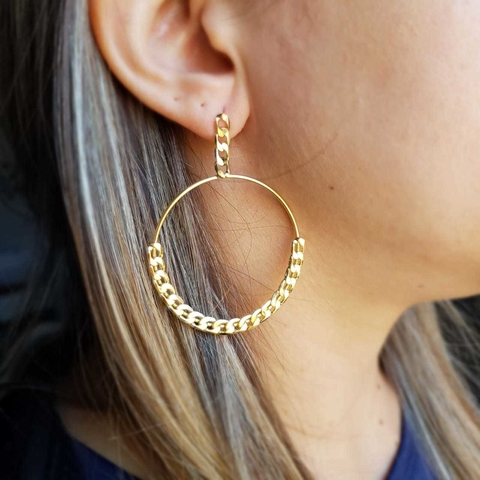 Brinco argola grande com detalhe em corrente folheado em ouro 18k, usado por uma mulher.