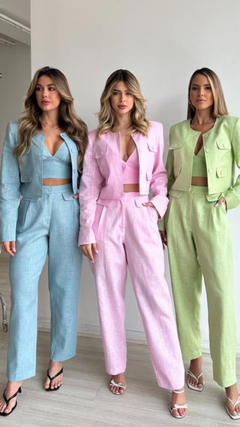 Três mulheres usando conjuntos coordenados com calças e casaquetos em cores pastel: azul, rosa e verde.
