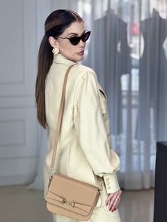 Modelo usando um blazer bege com botões dourados, acessórios elegantes e uma bolsa de ombro.