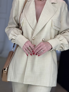 Blazer Genova em tom claro com botões dourados, modelo oversized, com detalhes elegantes e bolsos frontais.