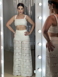 Modelo vestindo o Conjunto Estela Renda, composto por top e calça de renda branca, em frente a um espelho com luzes.