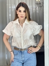 Model usando uma camisa Aura bordada de manga curta, com detalhes em renda, em um cenário iluminado.