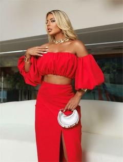 Modelo usando um conjunto vermelho com blusa de mangas bufantes e saia longa com fenda.