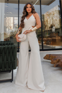 Modelo usando um macacão branco com recortes, posando em um ambiente moderno e elegante.