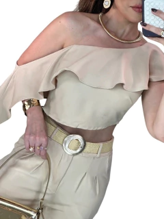 Modelo vestindo um conjunto cropped e calça alfaiataria em tom neutro, com detalhes em babados e acessórios em dourado.