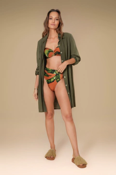 Modelo usando uma camisa de praia verde sobre um biquíni com estampa tropical, em um fundo neutro.