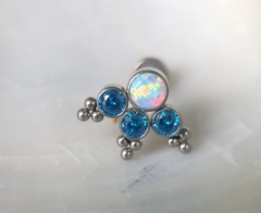 Piercing de titânio adornado com uma opala branca e três zircônias azuis (orelha)