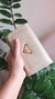 Carteira média dourada com textura, segurada por uma mão feminina, com detalhe de placa triangular da marca Miss Dong