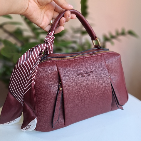 Bolsa maleta de mão ou transversal na cor bordô, com detalhes em couro e um lenço estilizado preso à alça.