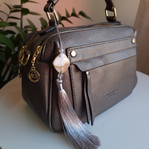 Bolsa baú média com alça de mão, detalhe do zíper e pingente decorativo.