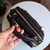 Bolsa baú média preta com alça de mão e zíper dourado, sendo segurada por uma mão.