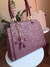 Imagem de uma bolsa feminina grande de ombro com alça trançada, na cor bordô, com um chaveiro em forma de urso; ao fundo, uma bolsa na cor nude.