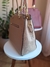 Imagem de uma bolsa feminina grande de ombro com alça trançada, na cor bordô, com um chaveiro em forma de urso; ao fundo, uma bolsa na cor nude.