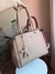 Imagem de uma bolsa feminina grande de ombro com alça trançada, na cor bordô, com um chaveiro em forma de urso; ao fundo, uma bolsa na cor nude.