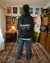Hombre de espaldas vistiendo un buzo negro de la marca Cuerdos en un ambiente decorado con posters y una tabla de surf.