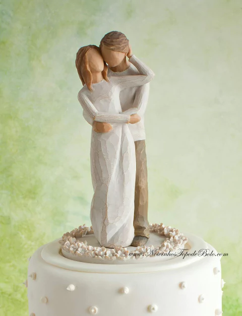 Topo de bolo rústico representando casal abraçado em figura esculpida em madeira clara sobre bolo branco decorado com pequenas pérolas