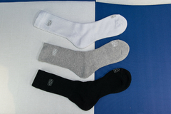 Medias de algodón en tres colores: blanco, gris melange y negro, sobre un fondo de color azul y blanco.
