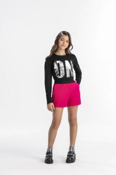 Modelo usando blusa juvenil de moletom preta com paetês e shorts rosa, em fundo branco.