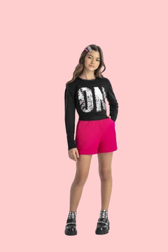 Modelo usando blusa juvenil de moletom preta com paetês e shorts rosa, em fundo branco.