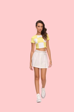 Modelo usando uma blusa cropped amarela com detalhes brancos e uma saia branca.