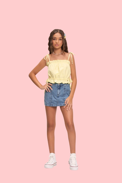 Modelo usando blusa cropped amarela e saia jeans, posando em fundo neutro.