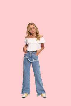 Modelo usando uma blusa cropped branca e calça jeans rasgada, com acessórios coloridos no cabelo.
