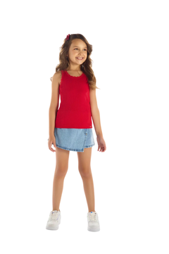 Menina sorrindo usando uma blusa feminina vermelha da Pulla Bulla, combinada com uma saia de jeans e tênis brancos.