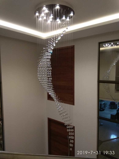 Um lustre de cristal em formato espiral, pendurado no teto, iluminando o ambiente com luzes LED.