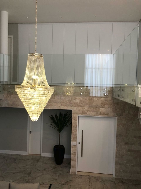 Um lustre de cristal elegante pendurado em um ambiente moderno, com paredes de pedras e um toque de natureza.