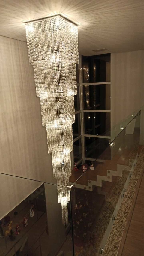 Lustre de cristal em formato quadrado, com várias camadas de correntes de cristal, iluminando um ambiente moderno.