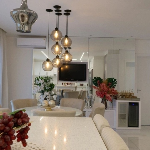 Decoração de sala com luminárias pendentes de vidro fumê, mesa de jantar e plantas decorativas.