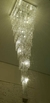 Lustre em cristal quadrado, com design em cascata e iluminação brilhante, suspenso em um ambiente moderno.