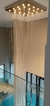 Lustre da Linha Cristal Safir com hastes pendentes iluminadas, instalado em um ambiente moderno com escada e piscina ao fundo.