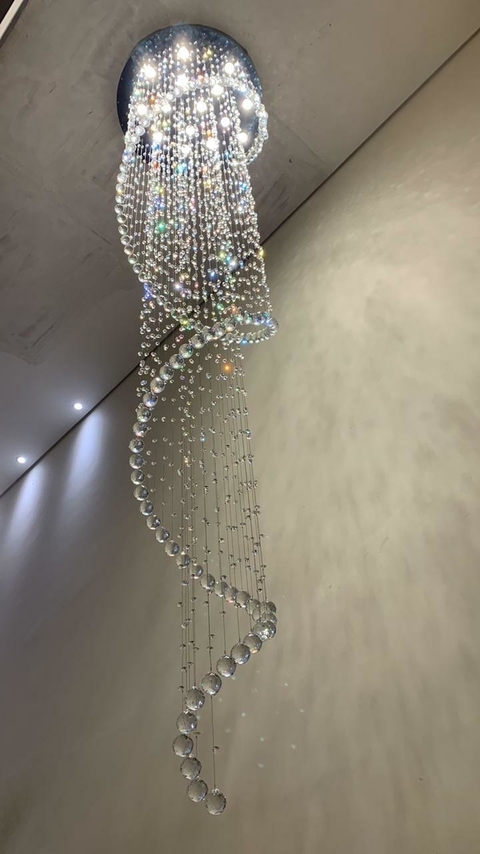 Um lustre de cristal em forma de caracol, com várias correntes de cristais que refletem luz, pendurado em um teto moderno.