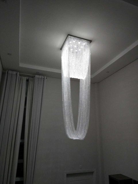 Um lustre elegante da Linha Cristal Paladino, no formato de véu de noiva, pendurado no teto de uma sala moderna.