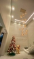 Ambiente decorado com uma árvore de Natal colorida e um lustre de vidro estilo conhaque pendurado no teto, ao lado de um ursinho de pelúcia.