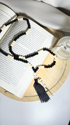 Japamala com contas pretas e claras, posicionada sobre um livro aberto, com um pequeno pompom na extremidade.
