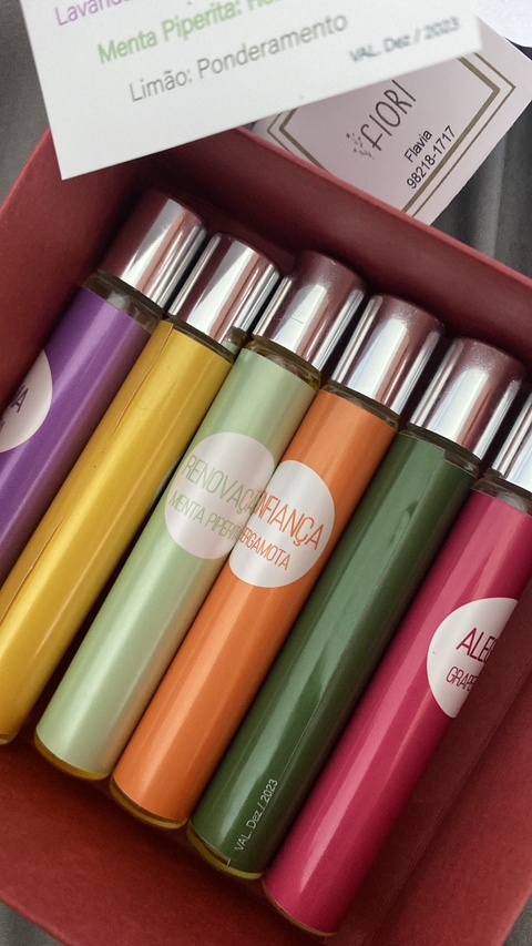 Conjunto de roll-ons de óleos essenciais em uma embalagem vermelha, com frascos coloridos e rótulos indicando os aromas.