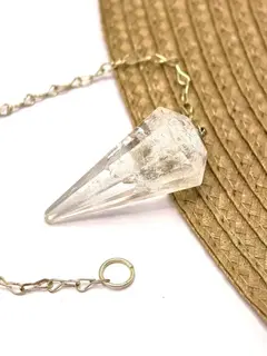 Pêndulo de quartzo cristal natural transparente com corrente metálica sobre superfície clara e tecido marrom