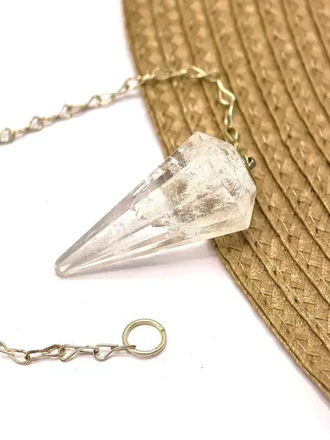 Pêndulo de quartzo cristal natural transparente com corrente metálica sobre superfície clara e tecido marrom