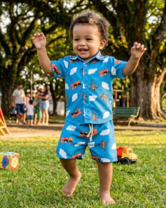 Menino pequeno sorridente usando conjunto azul com estampa dos personagens 3 palavrinhas deus e amor e desenhos coloridos, no parque